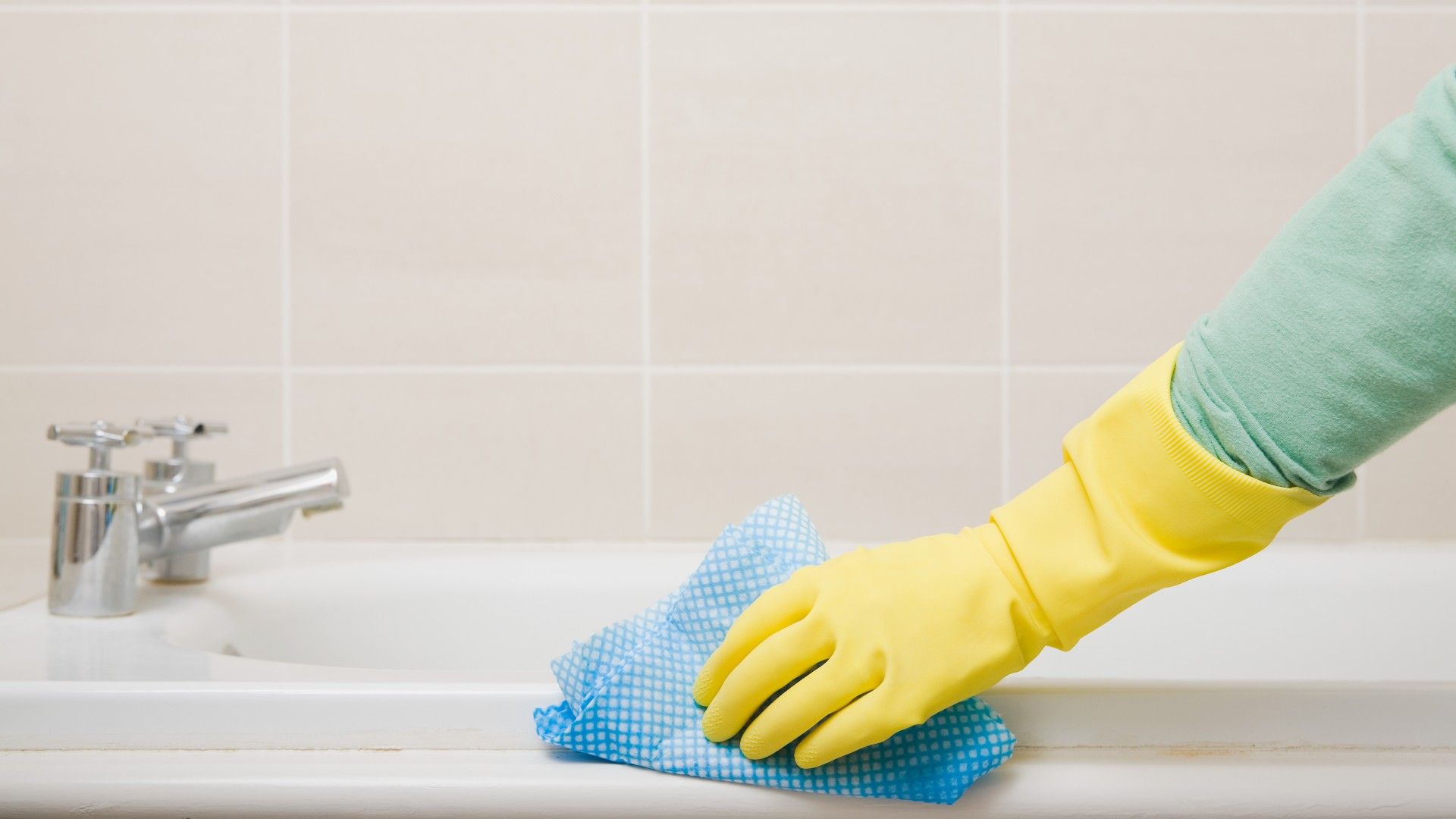 hand with a glove on using a cloth to wipe down a bathtub