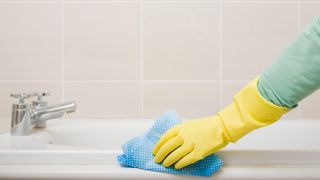 hand with a glove on using a cloth to wipe down a bathtub