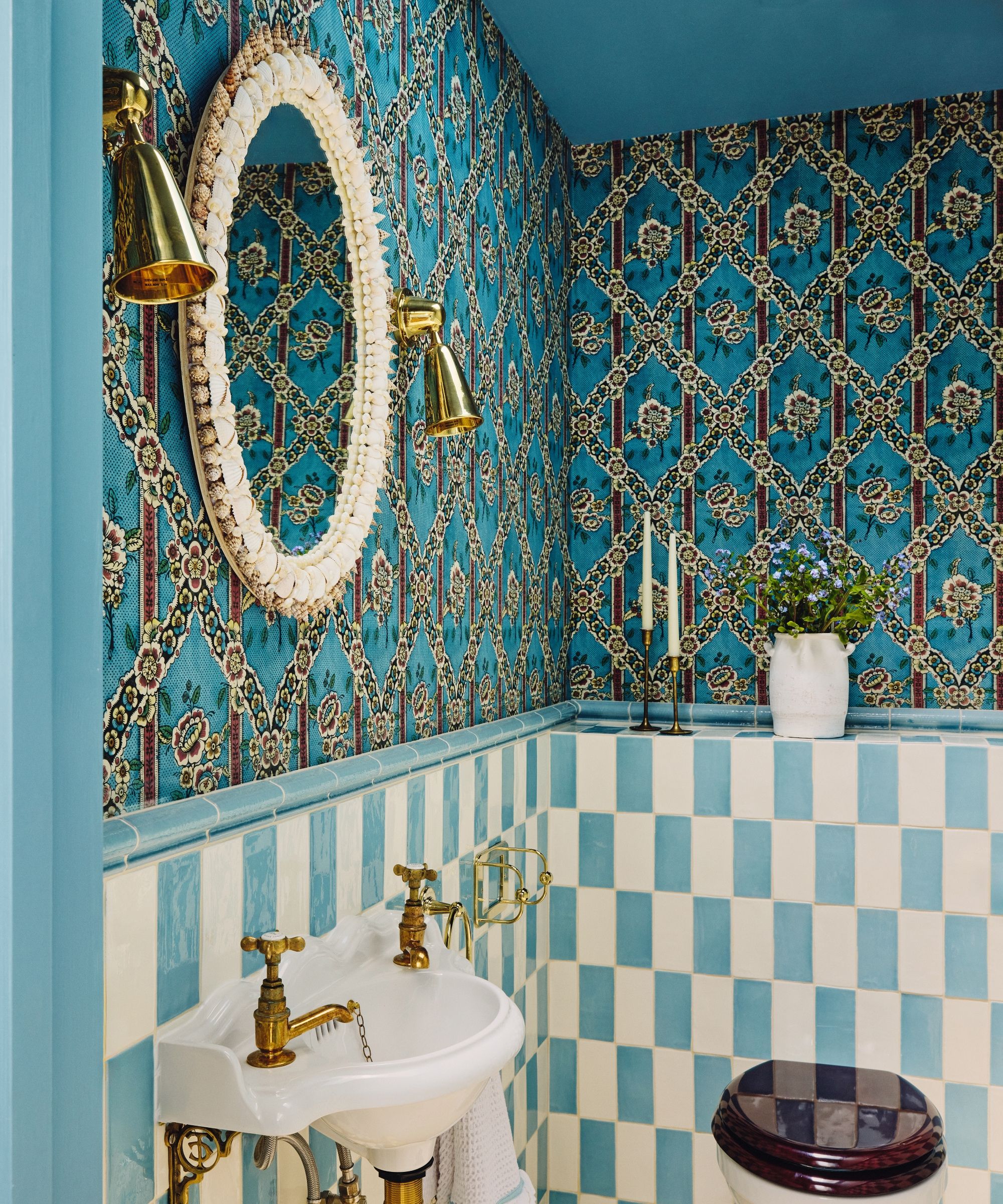 A guest bathroom with blue and white checkerboard tiles on the lower walls, a blue and red patterned wallpaper on the upper walls, and a white oval mirror