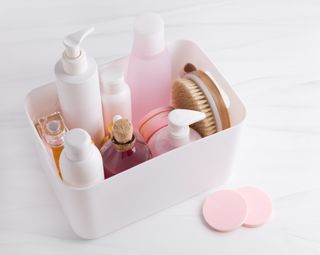 A pink plastic container filled with beauty products and toiletries on a marble surface