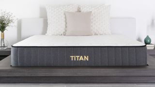 Best firm mattress: the Titan Plus mattress in a bedroom with a deep grey base and a white cover, dressed with luxury white and cream cushions