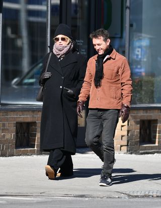 Jennifer Lawrence accessorizing a black Dior coat with a marled scarf, black leather tote from The Row, and black sneakers from Loewe.