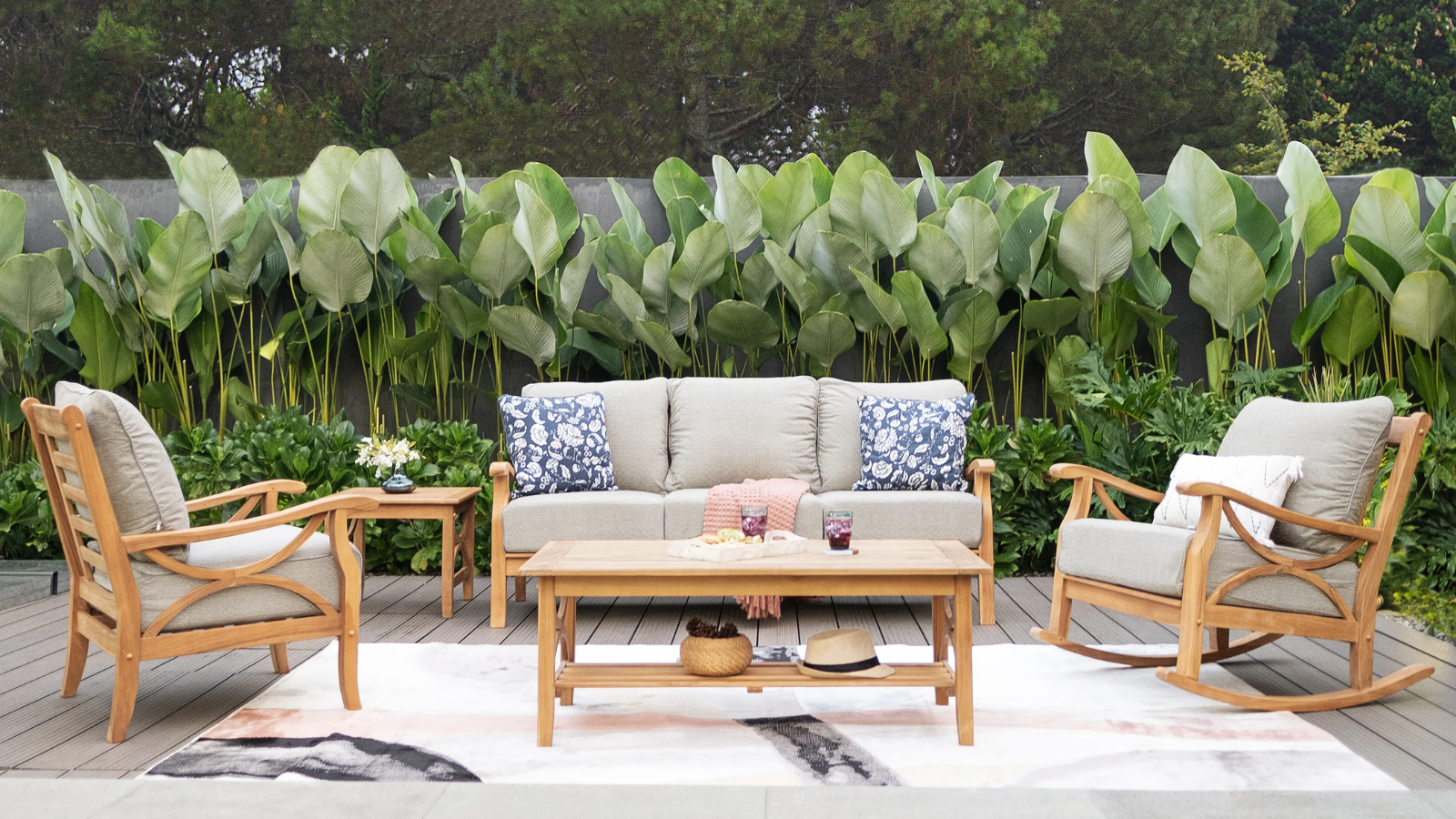 a patio set with a three seater couch, an accent chair, and a rocking chair all surrounding a coffee table and a large outdoor rug
