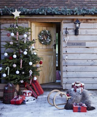 Christmas porch decor ideas with a fully decorated Christmas tree and a sled on the decking