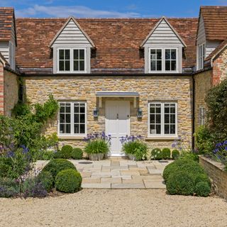 Cobbled cottage with patio slabs in front of the white front door and a gravel driveway