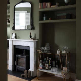 Living room wih dark green walls, period fireplace and shelving and drinks trolley in alcove
