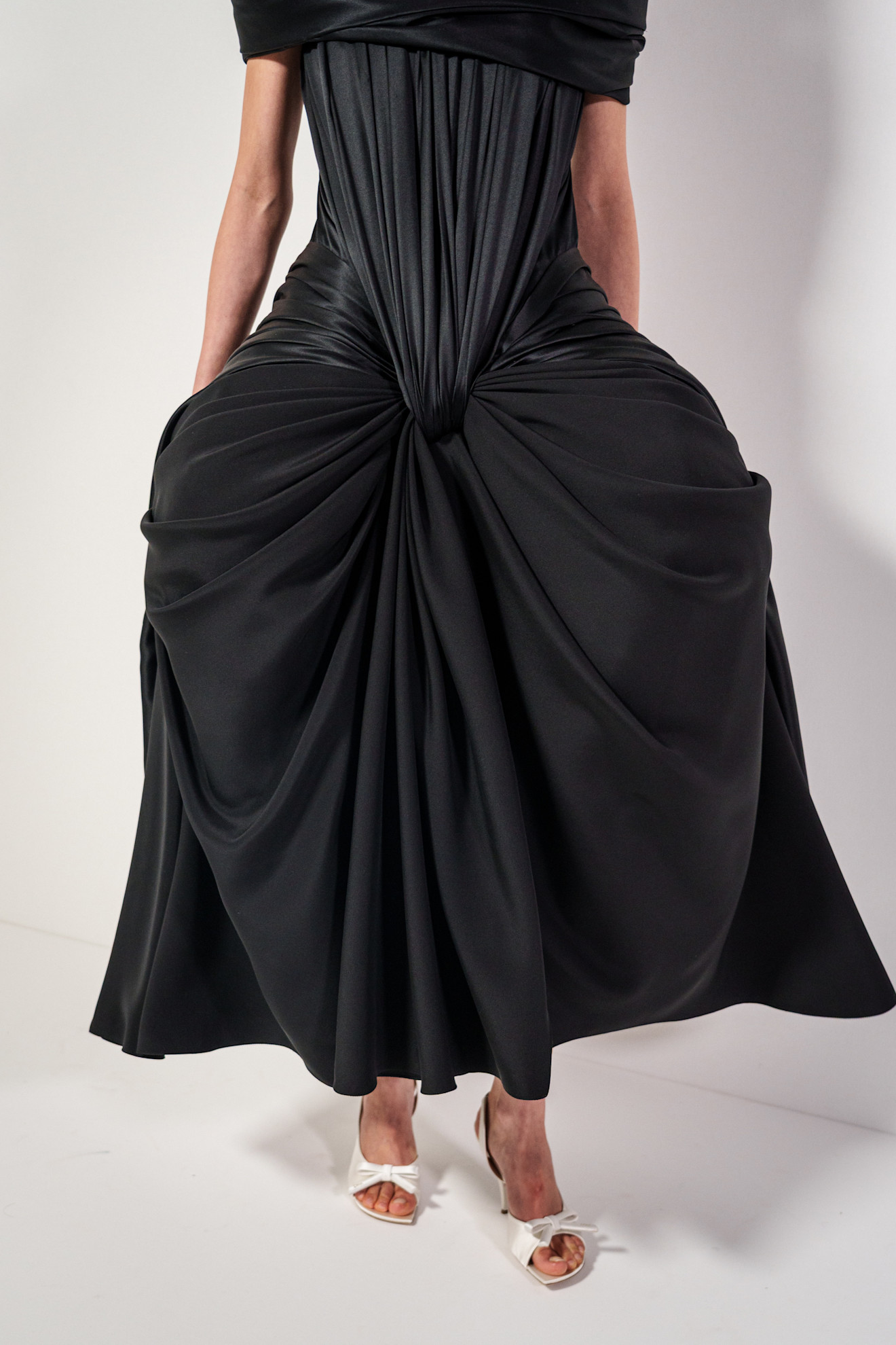 A Loewe model at the S/S 26 show wearing a black dress with white satin peep-toe heels.