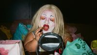 Colour photograph of a person applying lipstick in a small mirror