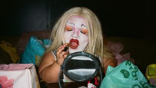 Colour photograph of a person applying lipstick in a small mirror