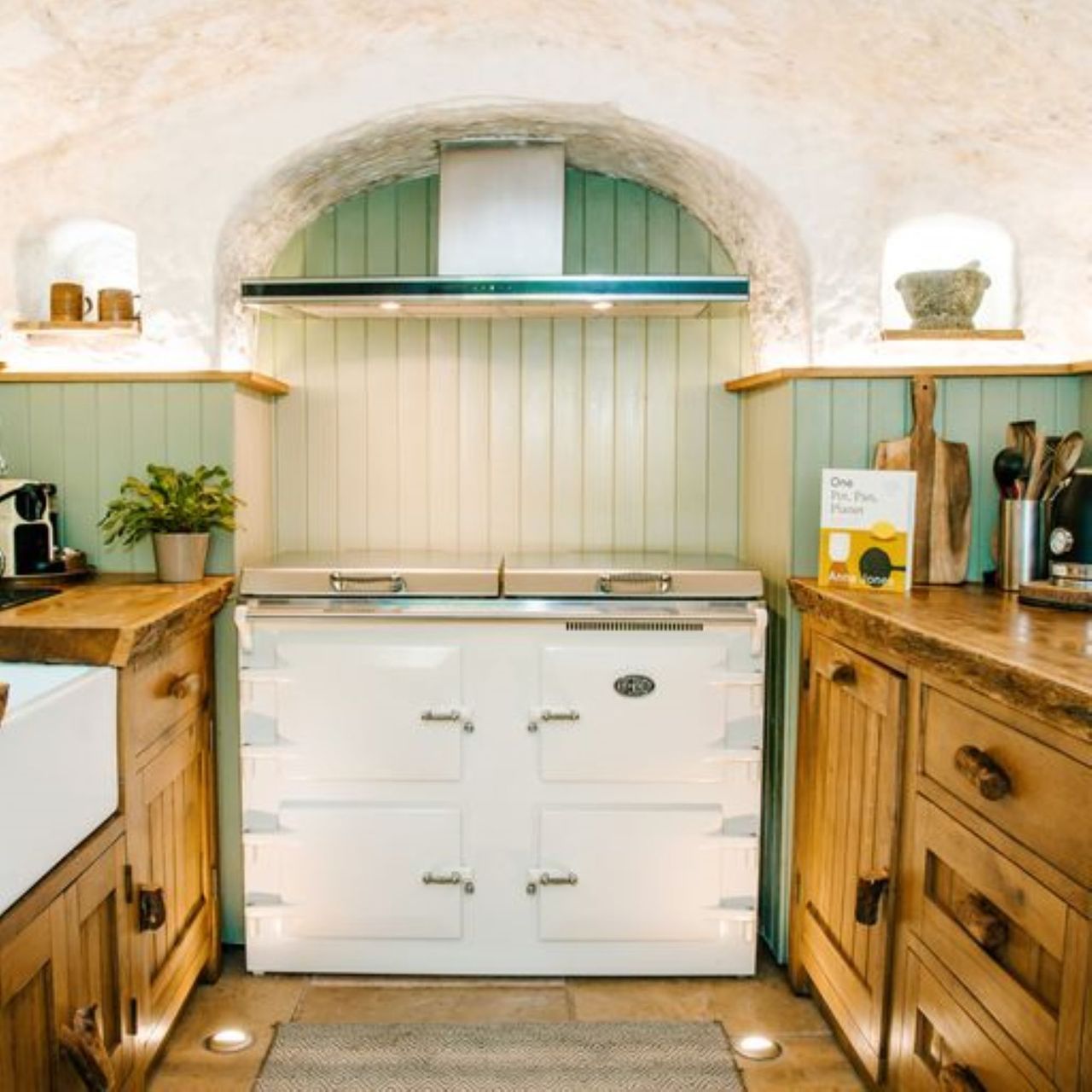 The kitchen includes a white oven and wooden worktops with stone walls covered in green wooden panels