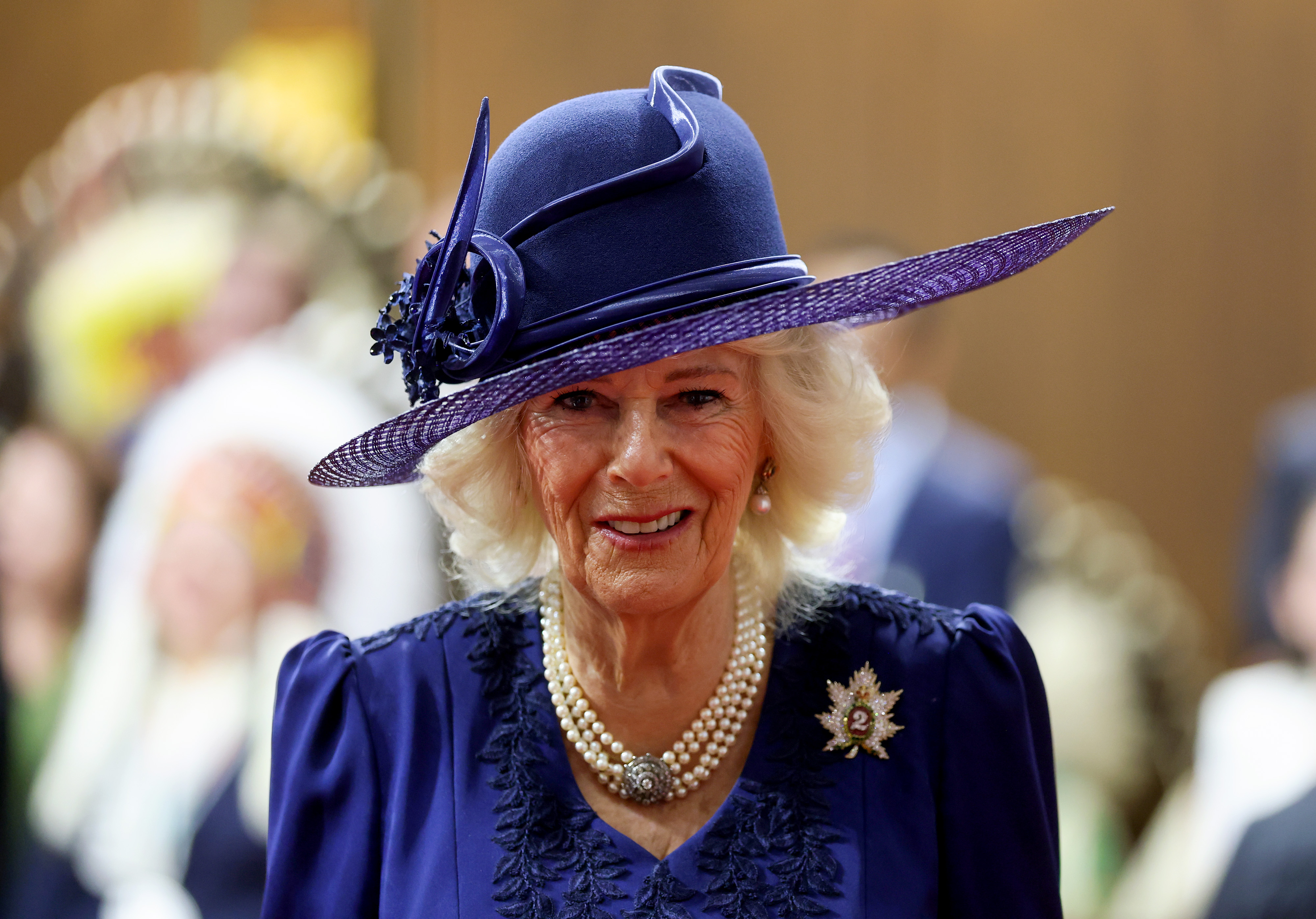 Queen Camilla wearing a blue dress and hat smiling
