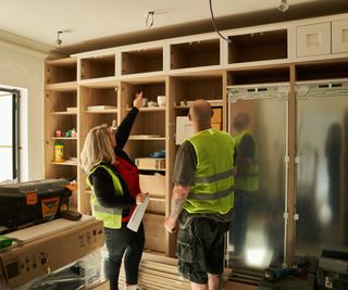 female and male wearing hi vis vests over work clothes looking at kitchen cabinets being fitted