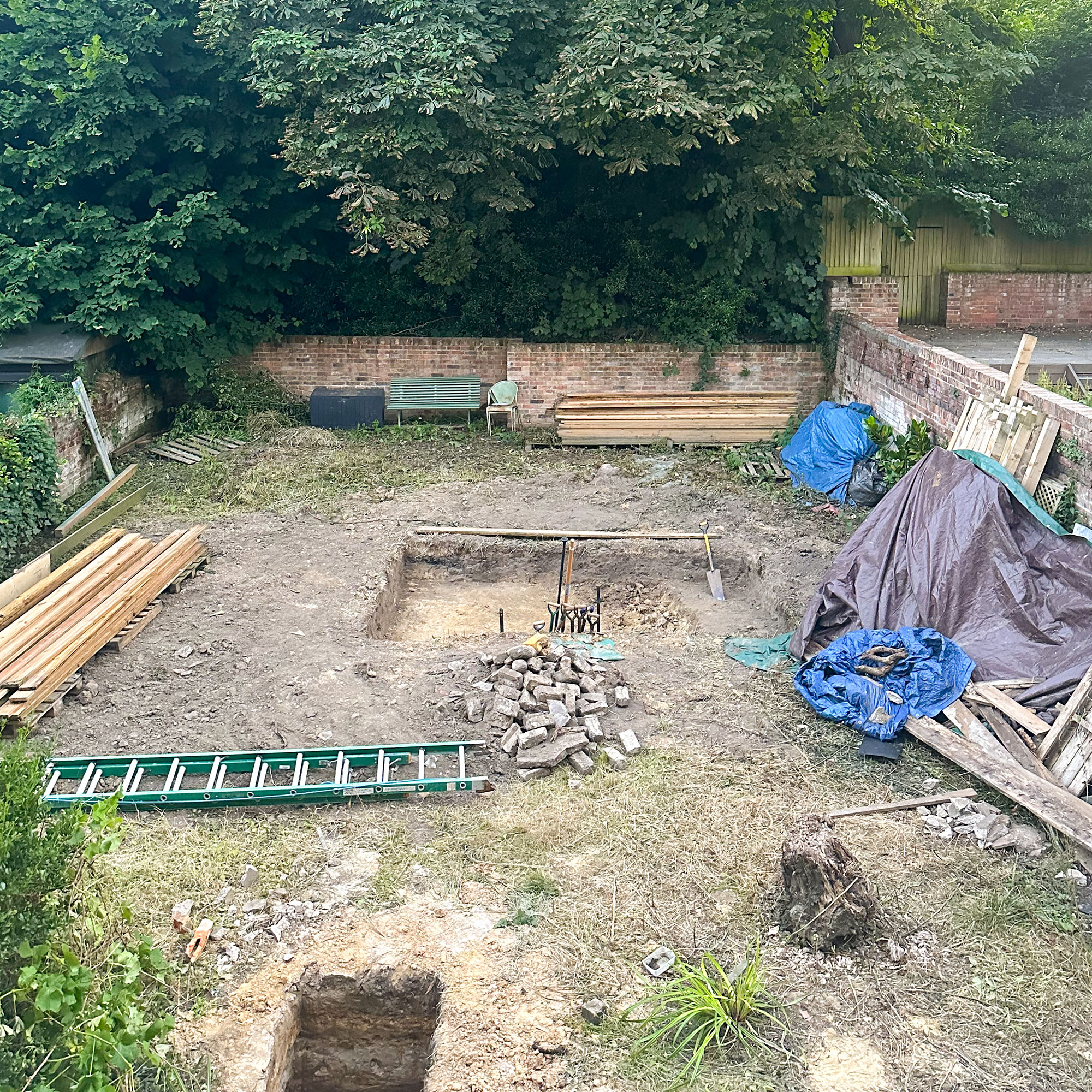 Back garden viewed from above, mid-renovation and landscaping, with holes dug and piles of timber stacked around