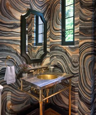 An example of powder room wall decor showing a dark powder room with swirly stone walls in black, orange and gray