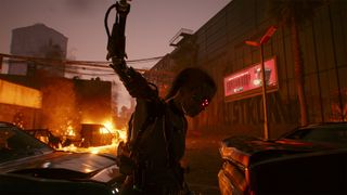 Cyberpunk 2077 netrunner builds - A punk with a cyberarm holds his fist up in front of burning cars