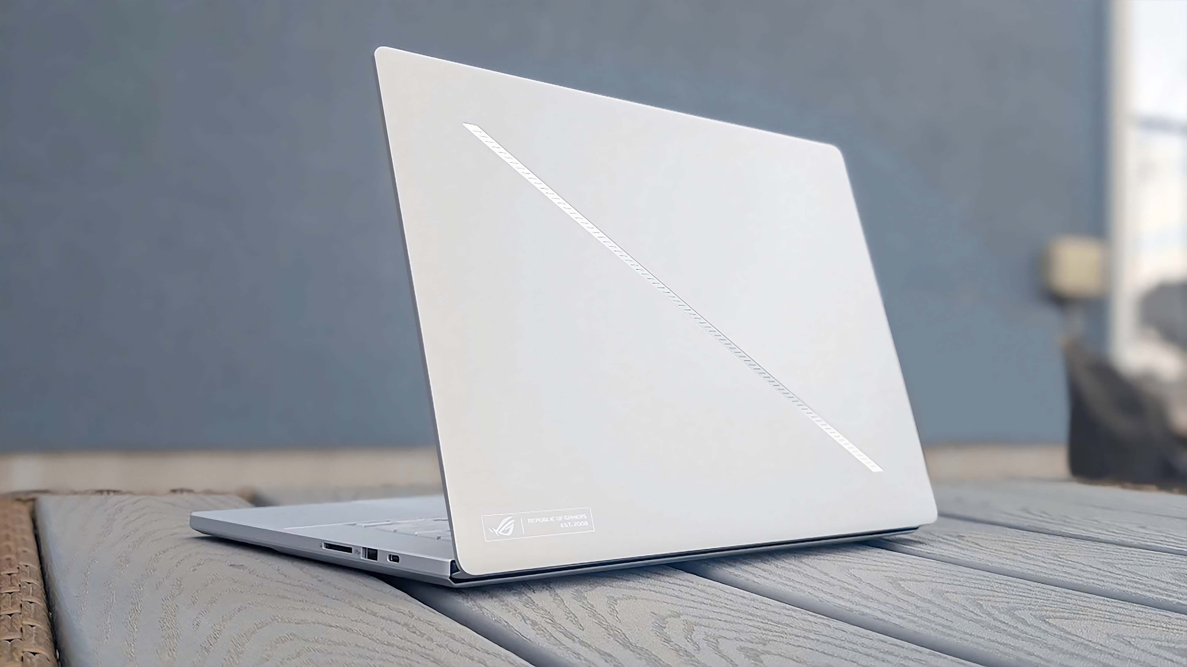The ASUS ROG Zephyrus G16 (GU605C, 2025) sitting on a grey table and facing away with the slash lighting on the lid.
