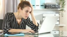 A young woman looks unhappy as she gazes at her laptop.