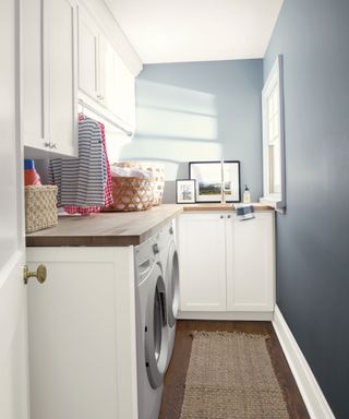 Small blue laundry room naturally lit by window, with natural runner on floor