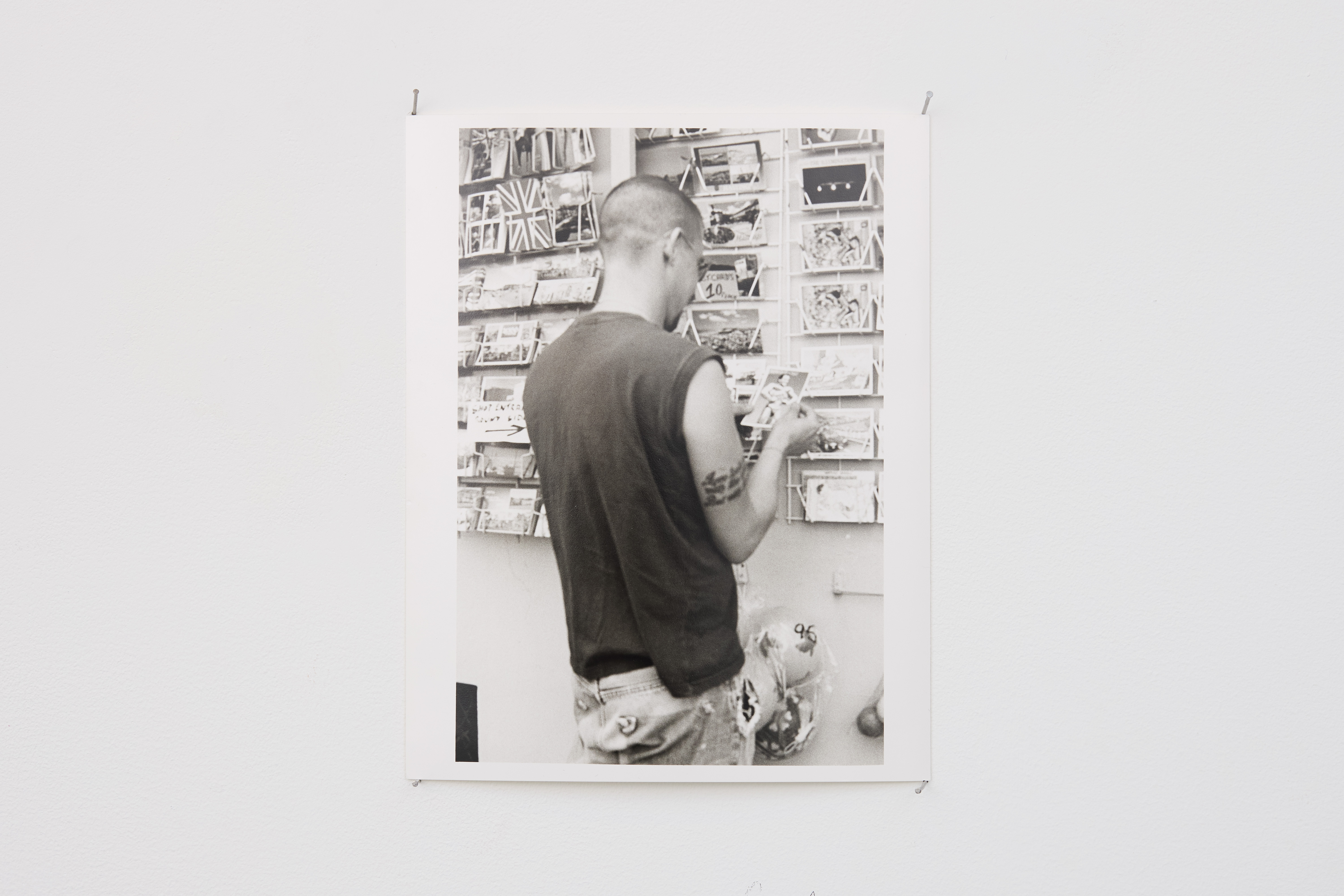 black and white photograph of person looking at postcards, pinned on wall