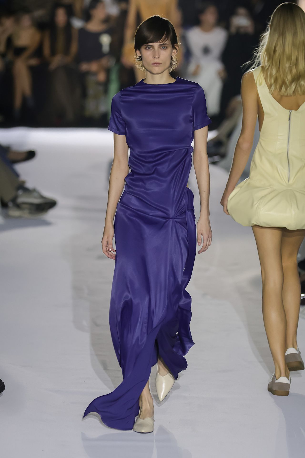 A Habey Club model wearing a dark purple silk gown styled with a pair of white pointed kitten heels.