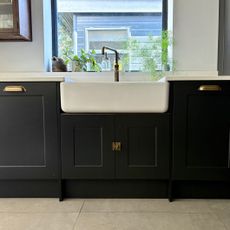 Dark grey kitchen cabinets with brass handles under a white double ceramic butler sink
