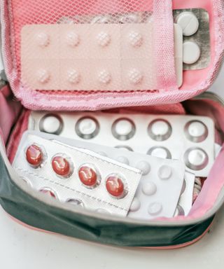 A pink and dark green bag that's open with silver medicine packets in it with white and red tablets inside