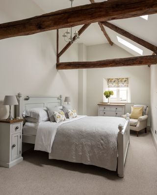 exposed wooden beams in vaulted bedroom ceiling with neutral walls and painted furniture and rooflights