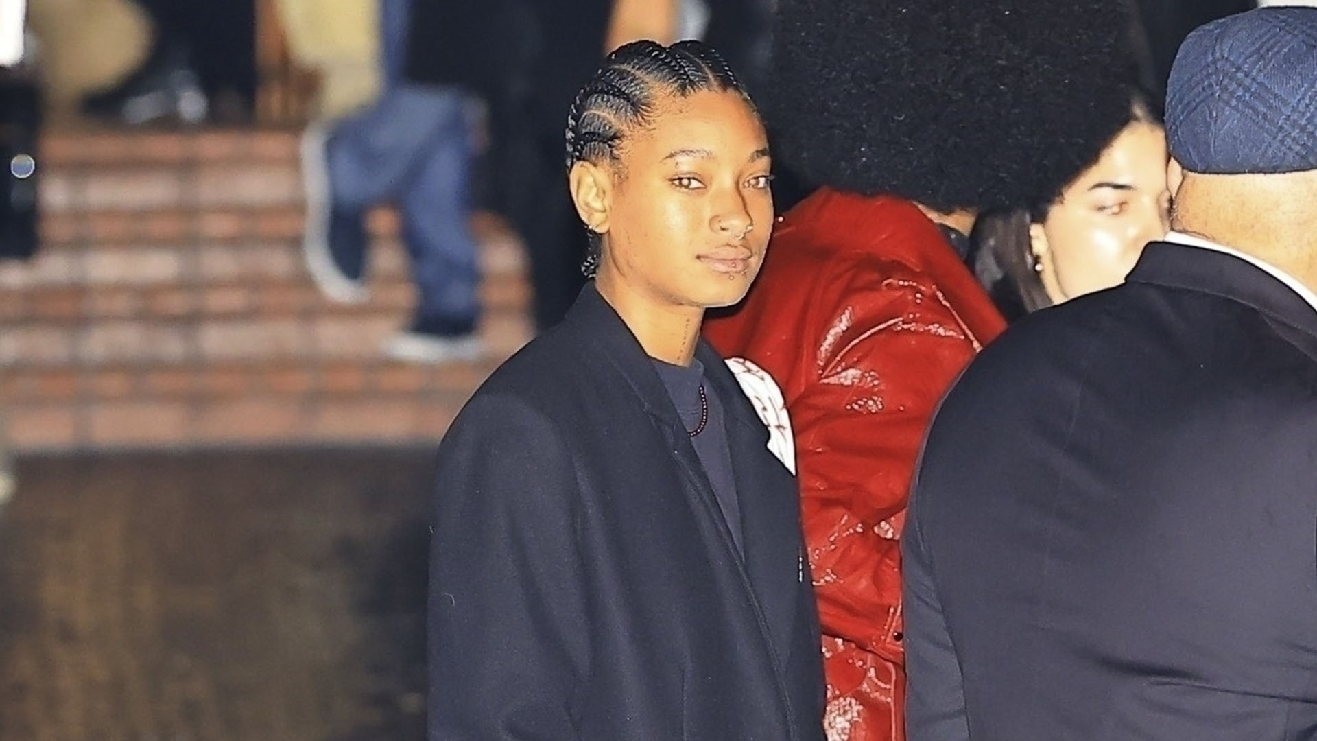 Willow Smith wearing a black coat, black boots, and short sweaterdress.