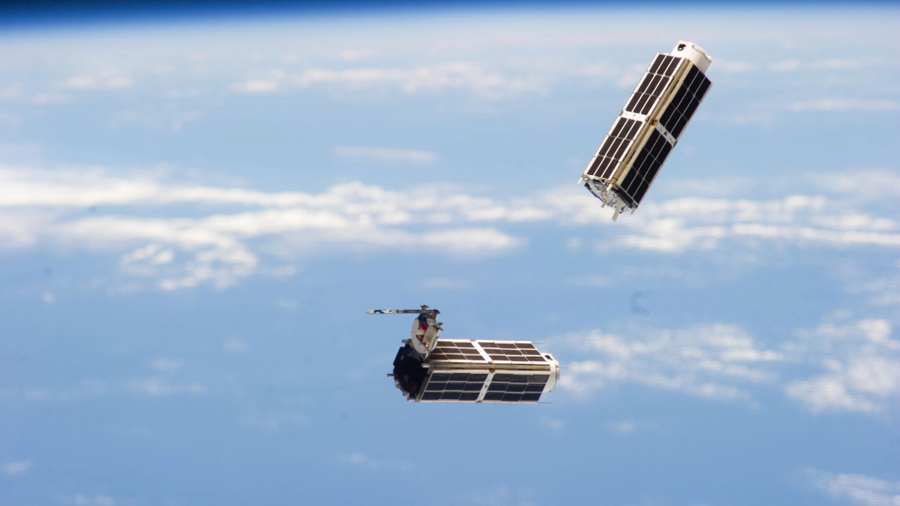Two small metal boxes float above Earth in space
