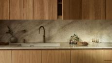 A kitchen with wooden upper and lower cabinets, with marble countertop and no handles and knobs