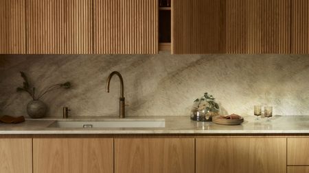 A kitchen with wooden upper and lower cabinets, with marble countertop and no handles and knobs