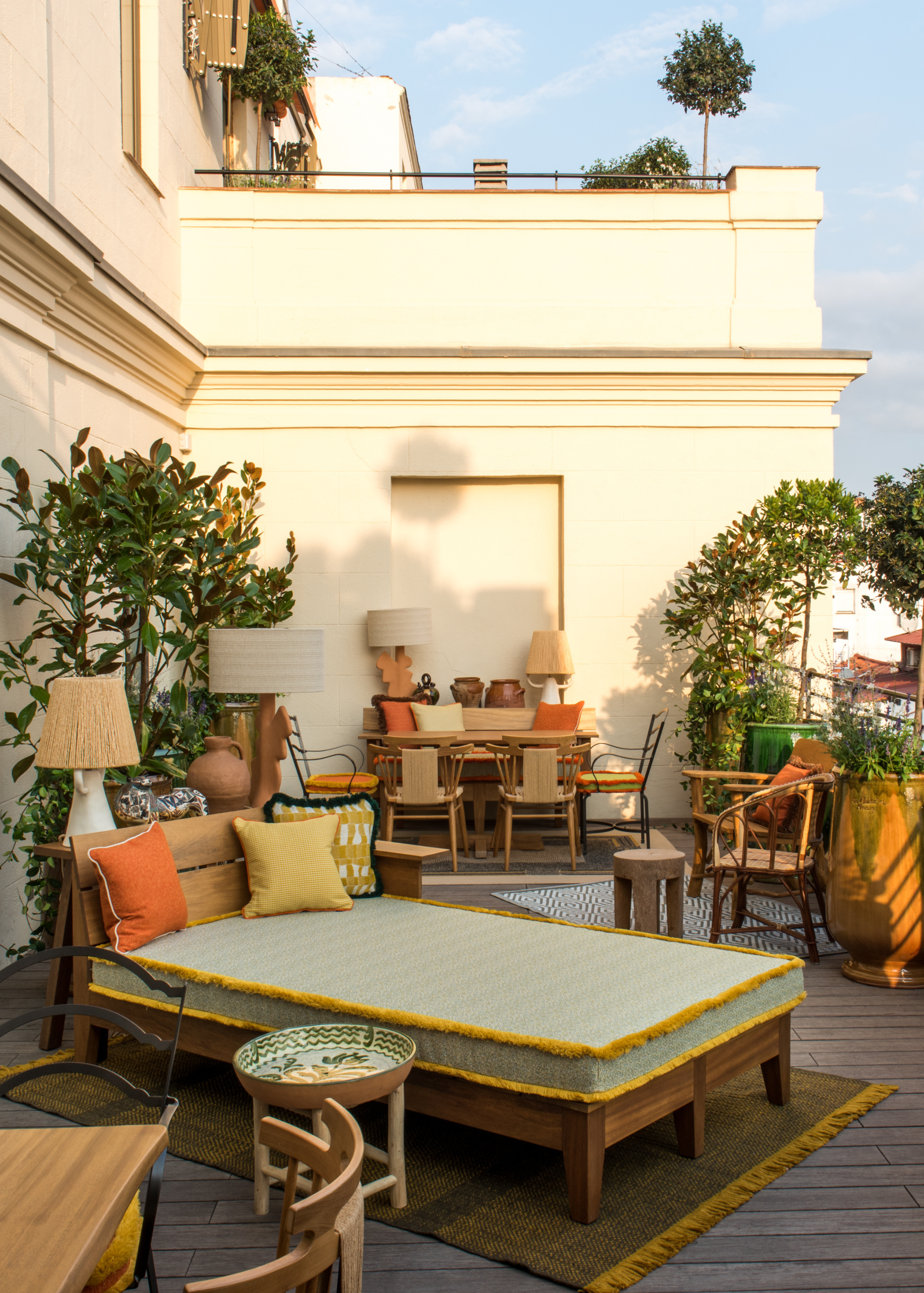 An outdoor balcony space attached to a hotel room with colorful lounging day beds, statement lamps and plenty of potted foliage