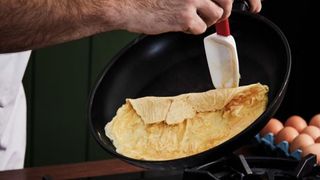 Hands using plastic spatula to fold omelette in half