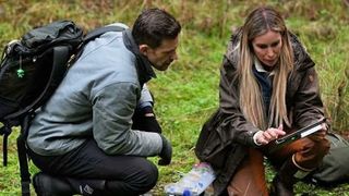 Bryce and Mireya crouch down in the forest to examine samples in a scene from Expedition Bigfoot season 5