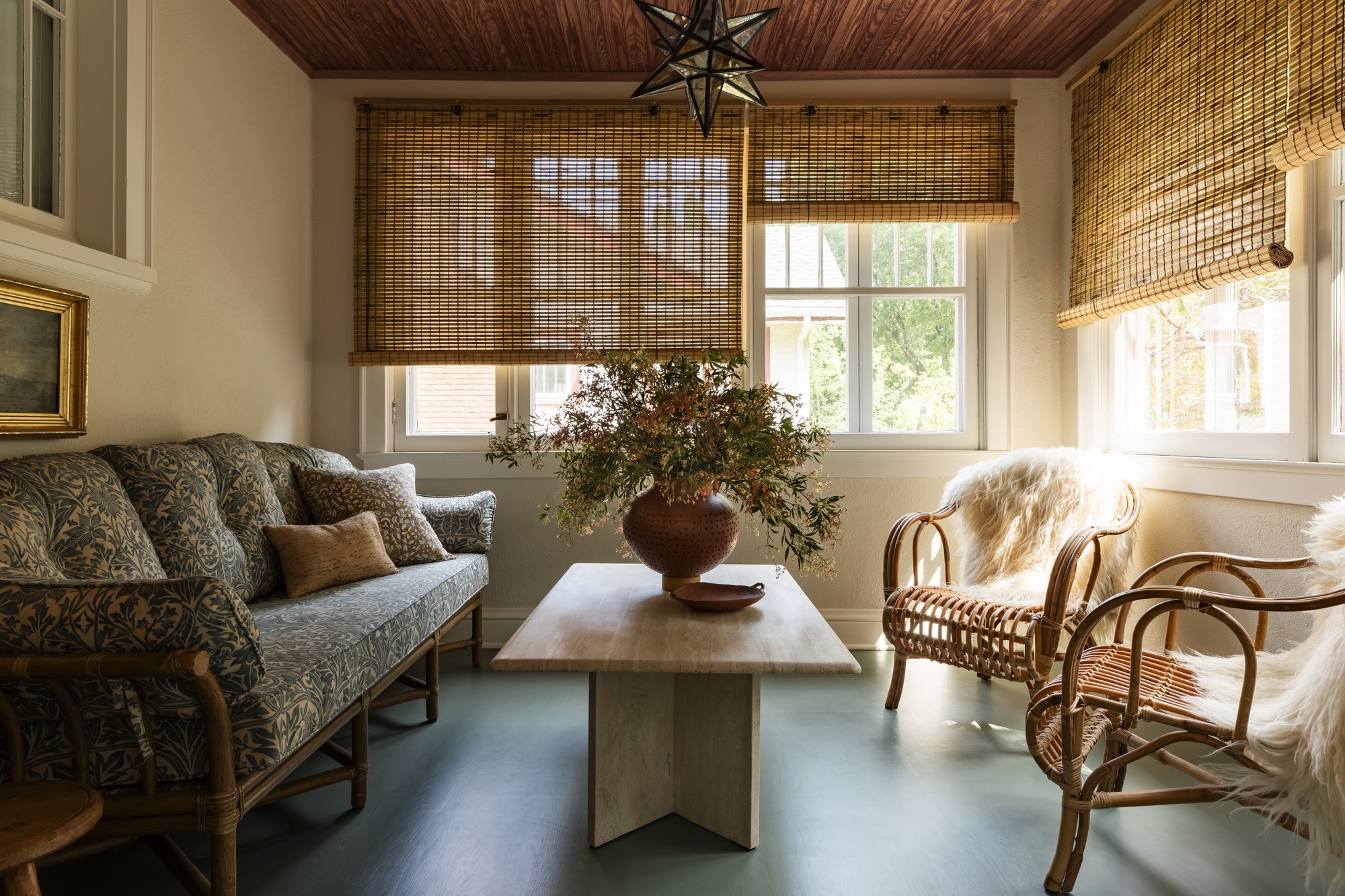 sunroom with bamboo blinds, patterned cane sofa, travertine coffee table and two rattan armchairs with sheepskin throws