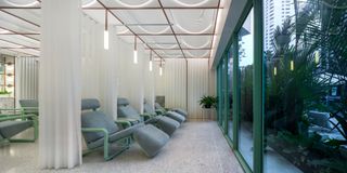 Treatment area with chairs, white curtains, terrazzo floors and view of outside greenery at Infinity Wellbeing, Bangkok
