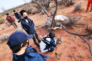 JAXA personnel inspect Hayabusa2's return capsule against the red soil of the Woomera Prohibited Area in Australia on Dec. 5.