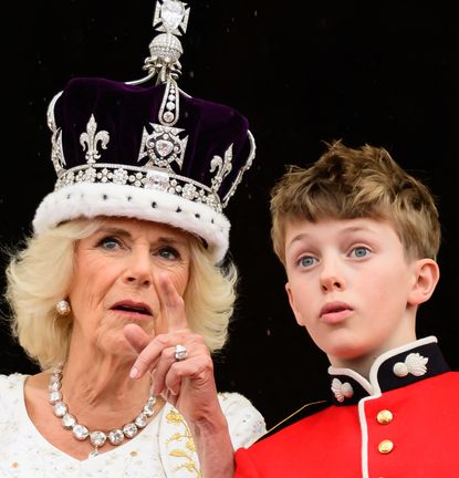 Queen Camilla wearing her coronation crown pointing at something to her grandson Freddy Parker Bowles