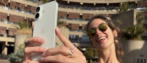 Person holding up an Apple iPhone 16 in both hands to take a photo and smiling widely