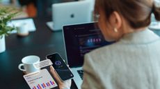 An office worker uses AI on her phone while sitting at her desk and laptop.