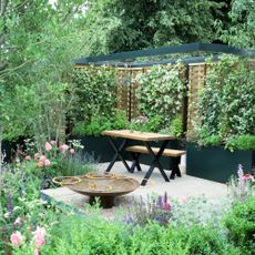 small garden with plenty of vibrant perennials planted in containers, bench and outdoor table, and water feature