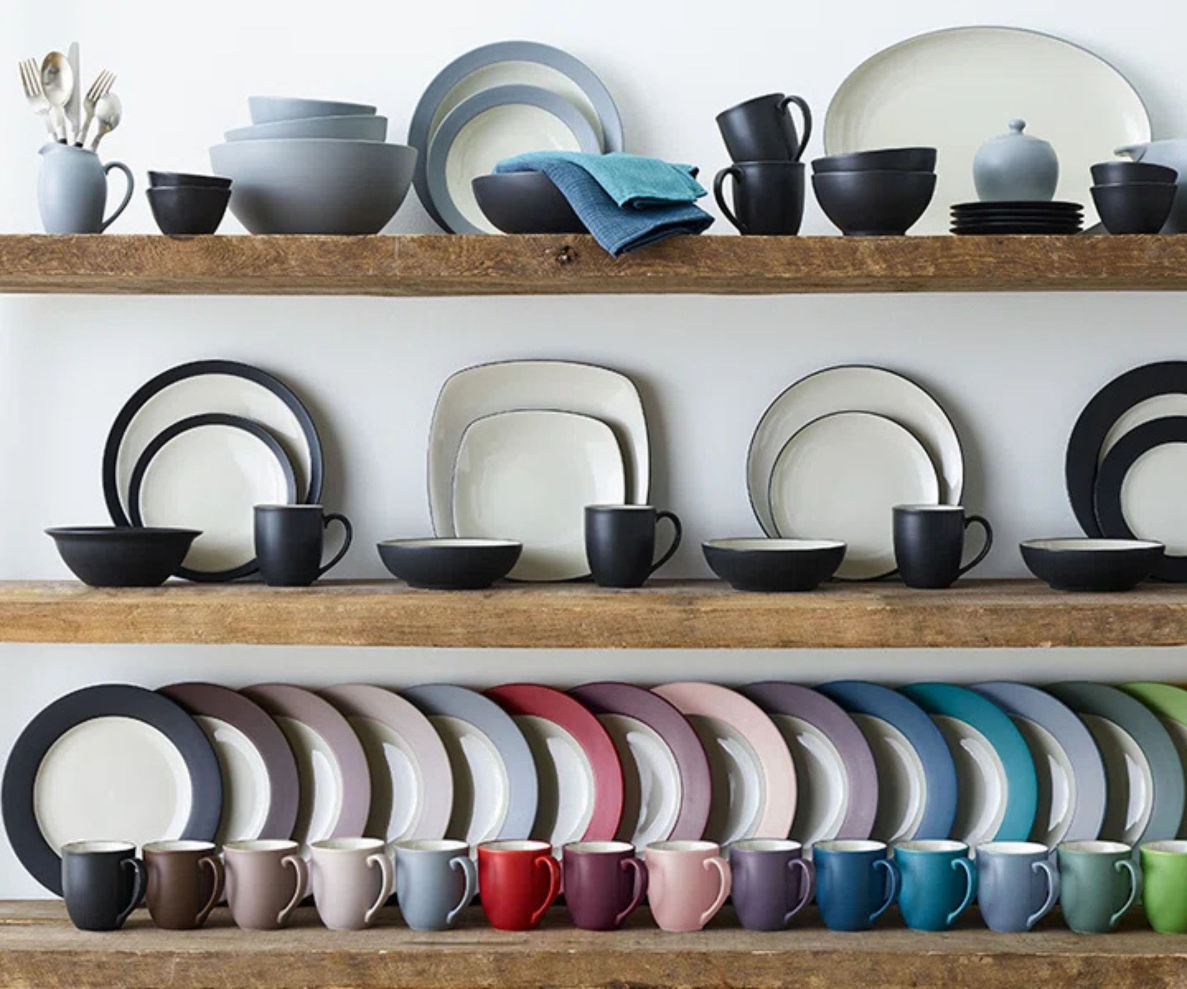 Three wooden wall shelves stacked with Noritake plates, bowls, and mugs in various colors