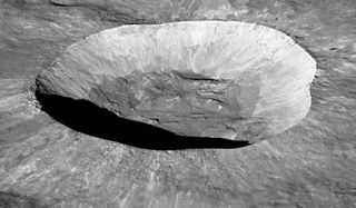 oblique view of a moon crater. the crater is pretty round and has a deep shadow on the front edge. surrounding it is higher moon terrain and above is black sky