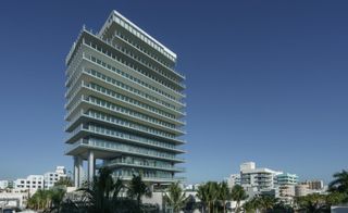 Lower level view of Rene Gonzalez’s crystalline tower. A high-rise building with glass banisters and palm trees in front of it.