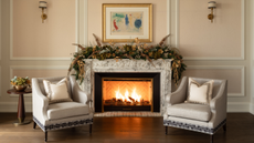 A living room area with a fireplace in the middle of two arm chairs and a garland above the fireplace as well as framed artwork