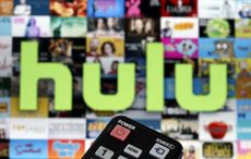 A remote control is seen in front of a television screen showing a Hulu logo.