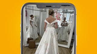 An iPhone on an orange background showing a woman wearing a wedding dress standing in front of two mirrors