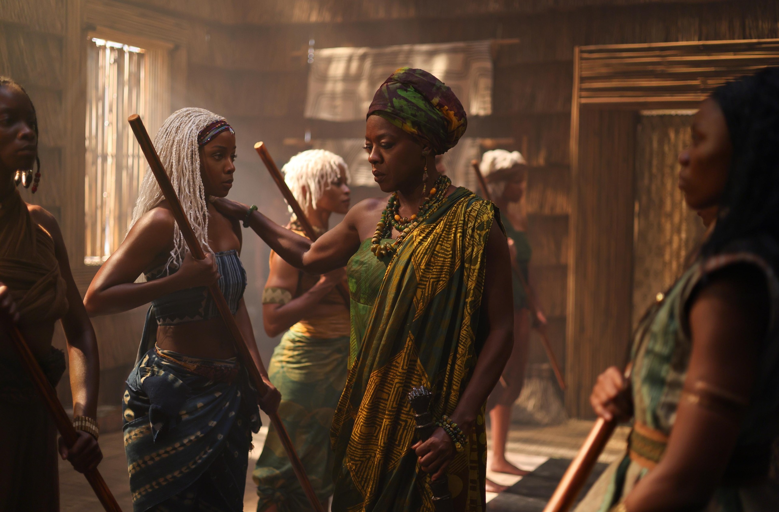 Viola Davis as Mama Agba in a room with younger women holding wooden staffs. She rests her hand on Thuso Mbedu as Zelie in still from 'Children of Blood and Bone.'