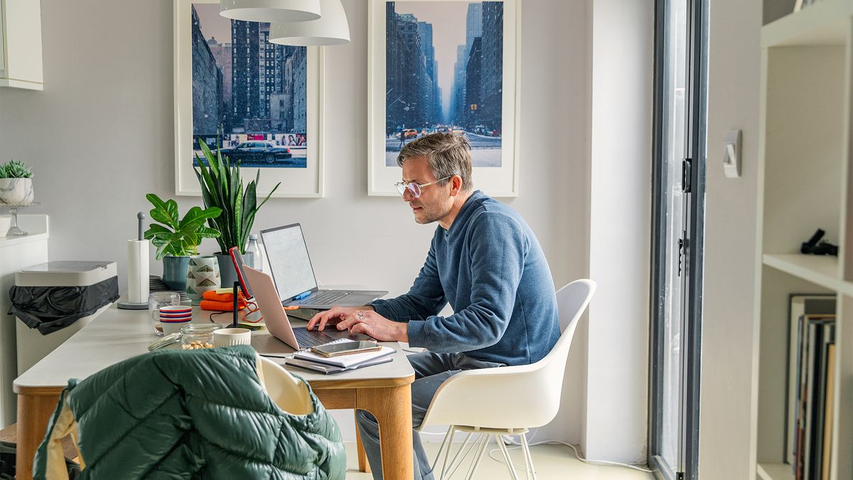 Flexible working concept image showing man working at a kitchen table in his home.