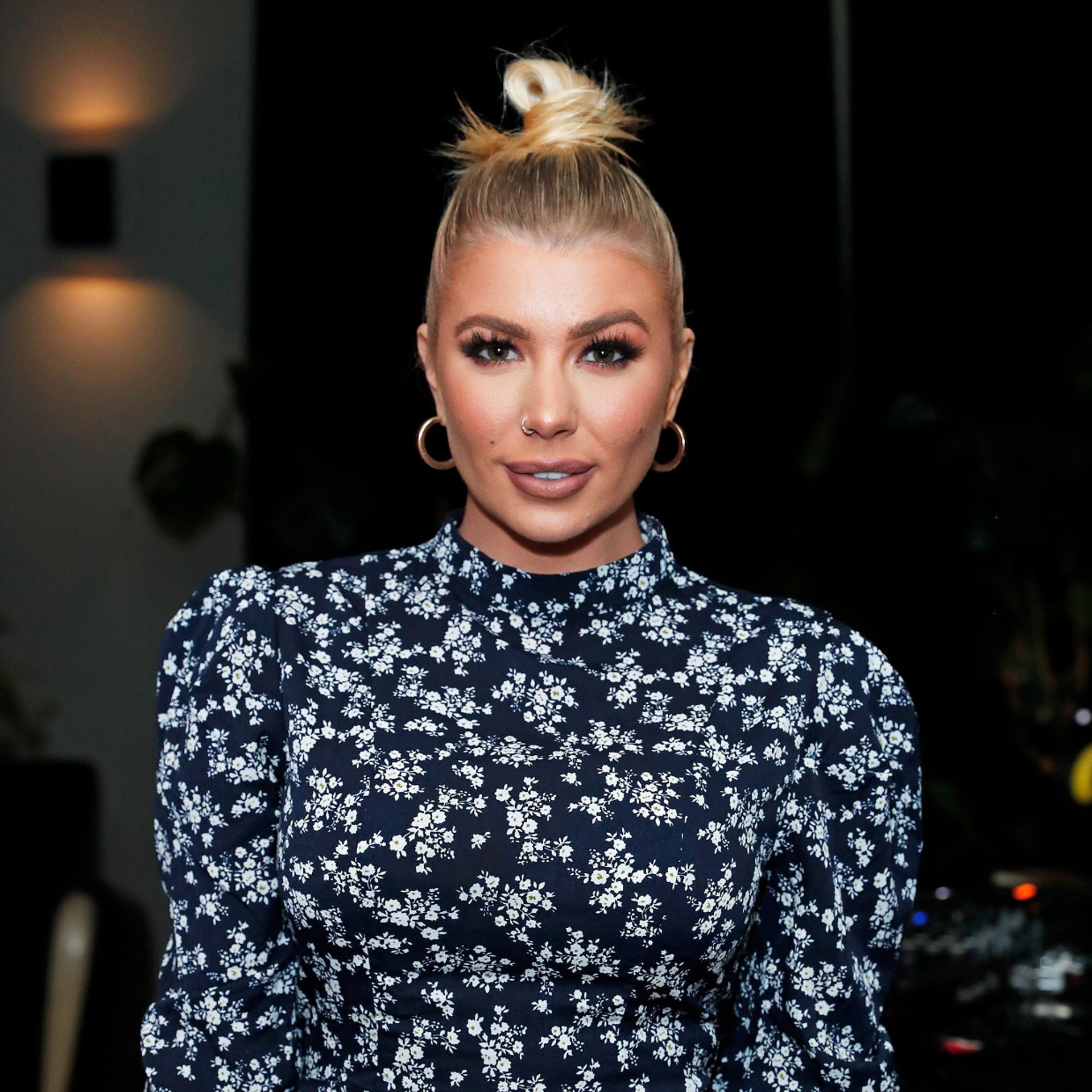 Woman with blonde hair in a high bun, wearing makeup and nose ring